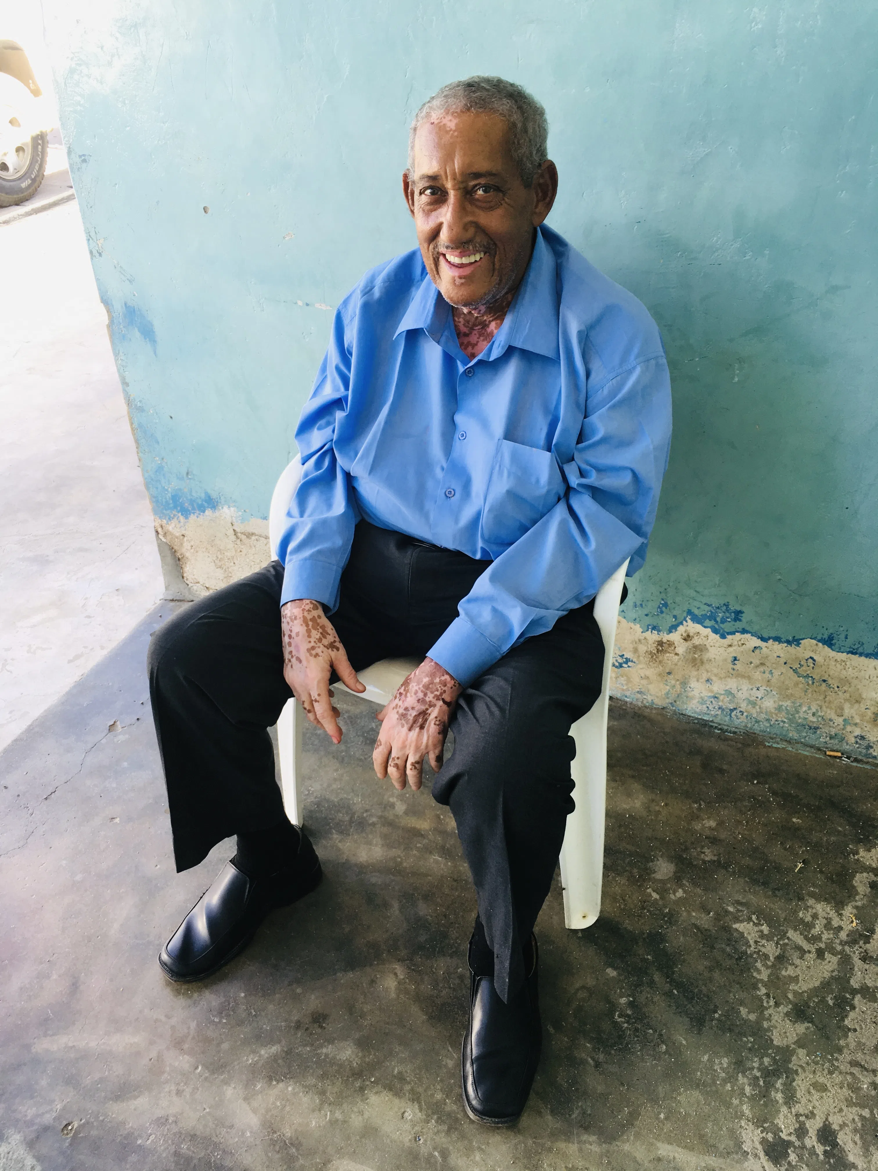 An older man seated against a pale wall