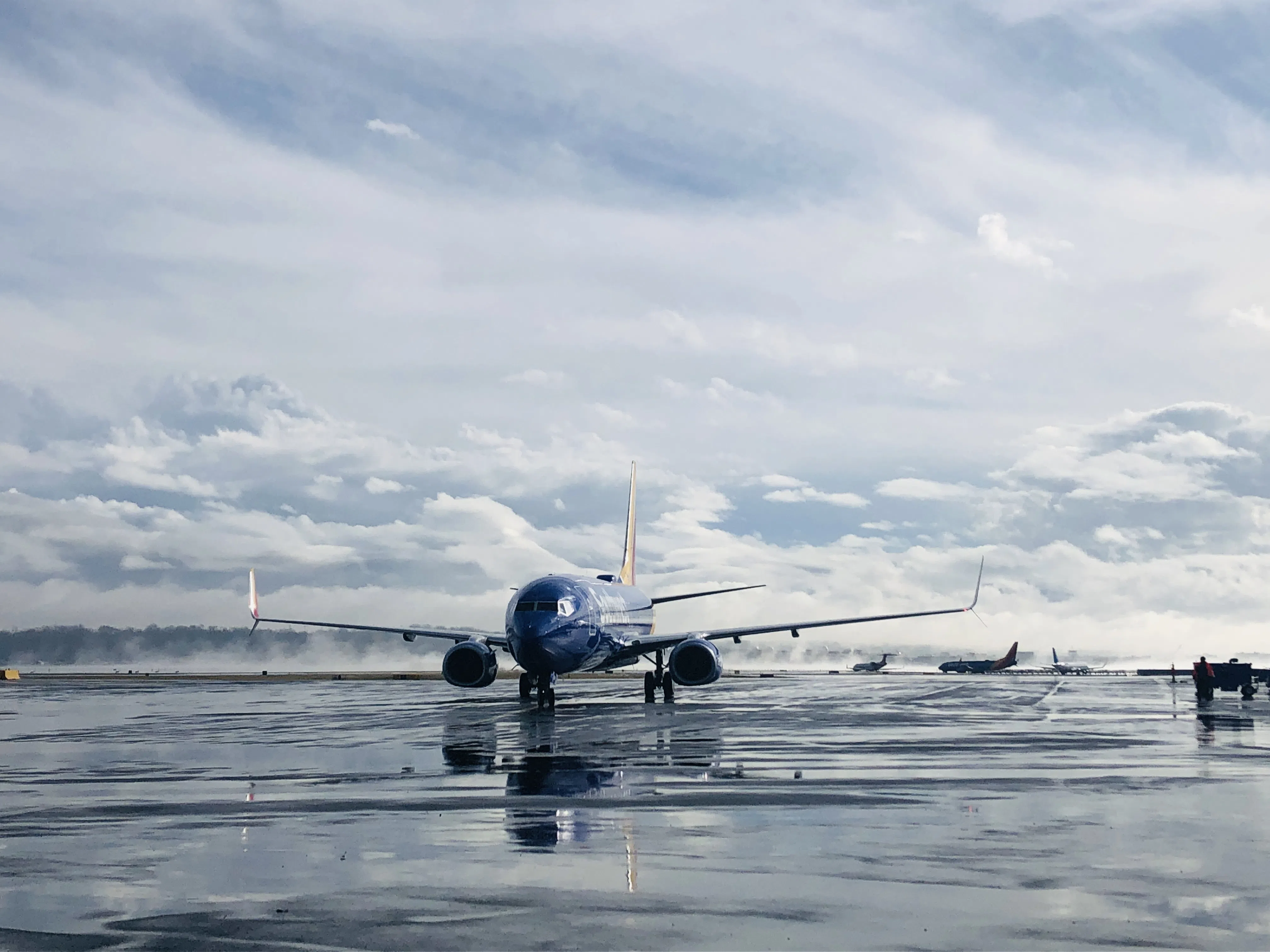 A commercial aircraft on a wet airport apron beneath dramatic clouds