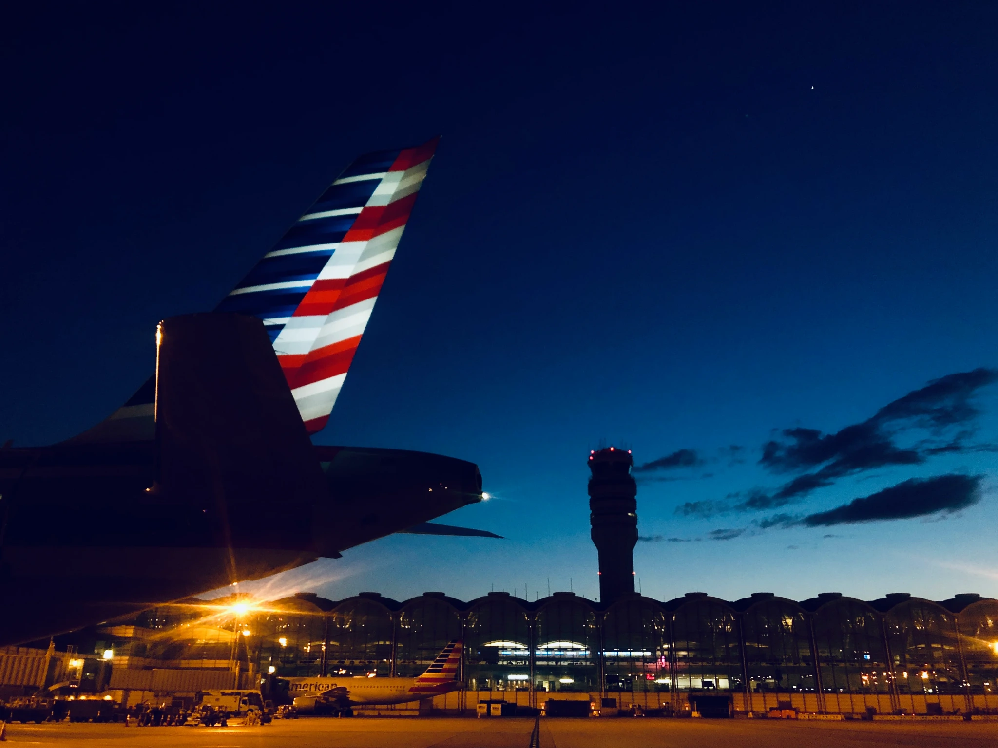 An American Airlines tail silhouetted against a deep blue airport night sky