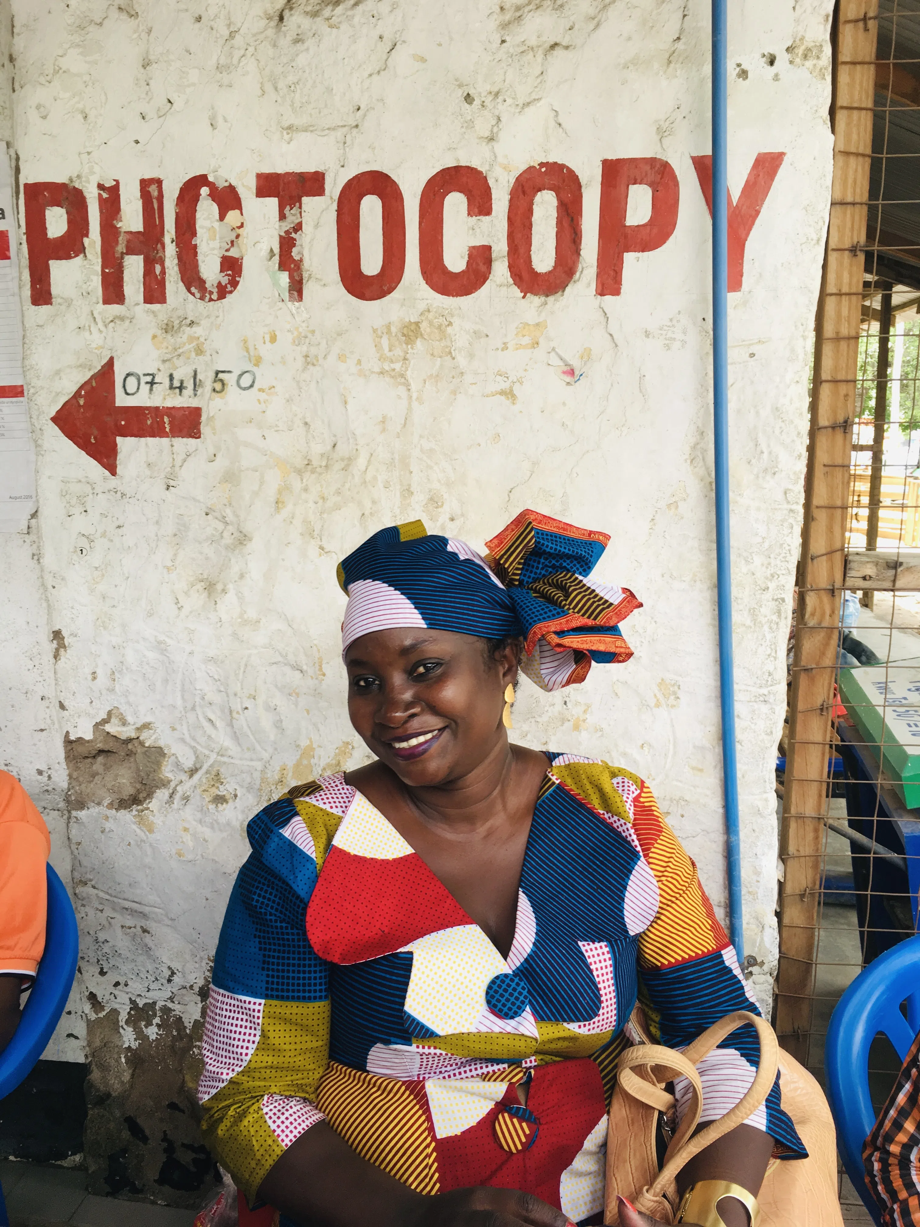 A woman in colorful clothing seated against a street-side wall