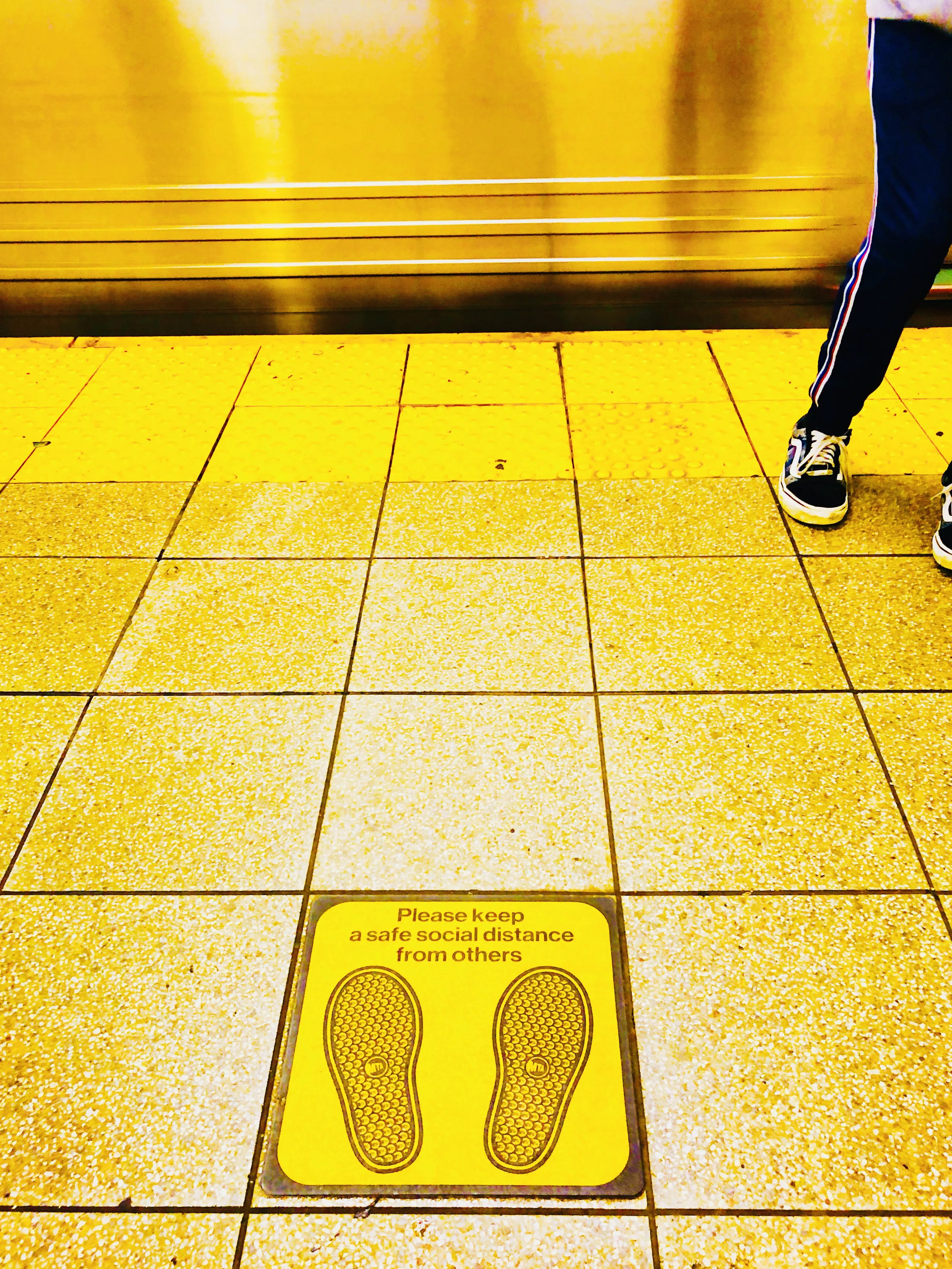 A transit platform with floor markings and a passing pedestrian