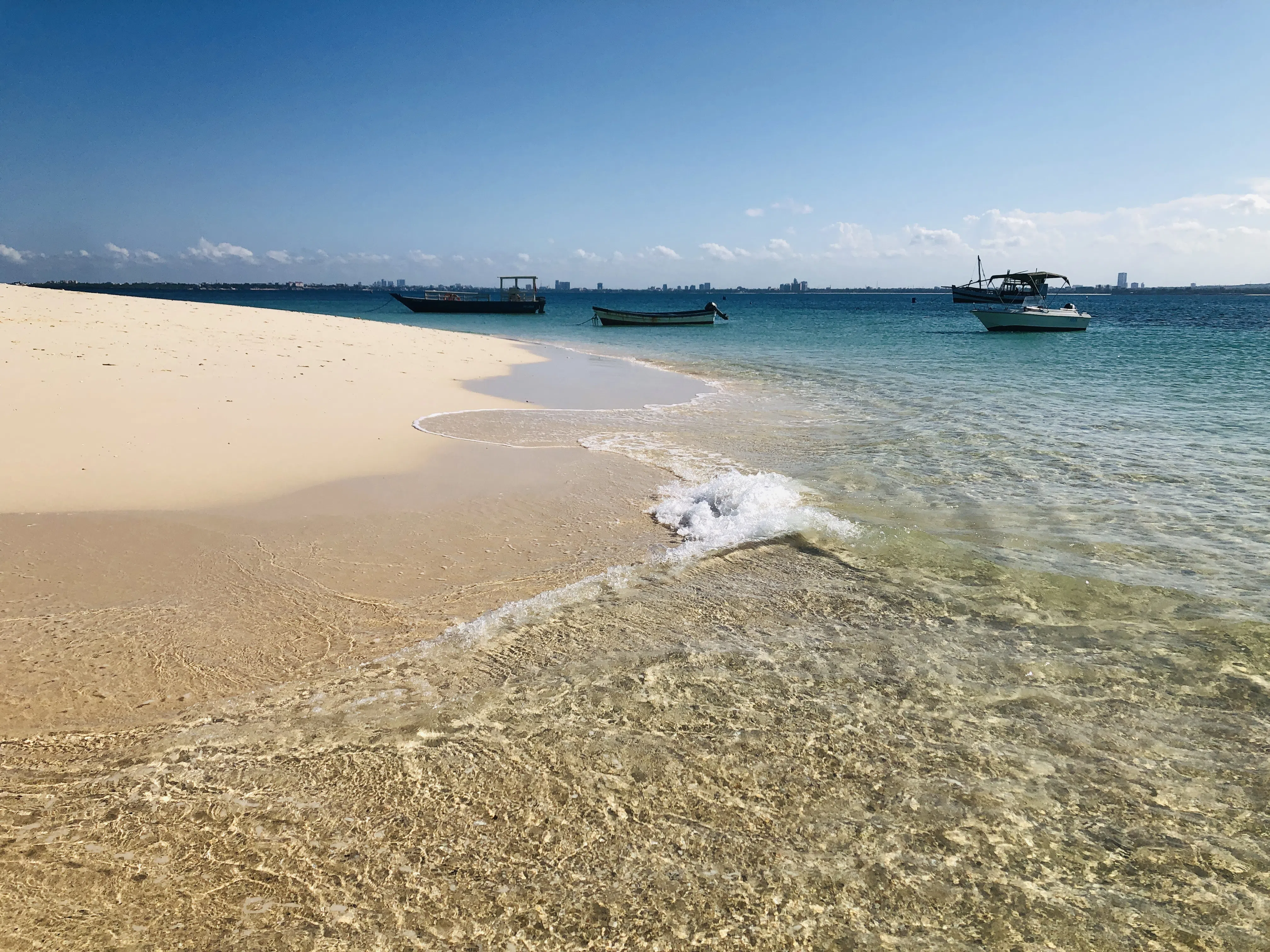 A bright tropical beach with clear water and boats offshore