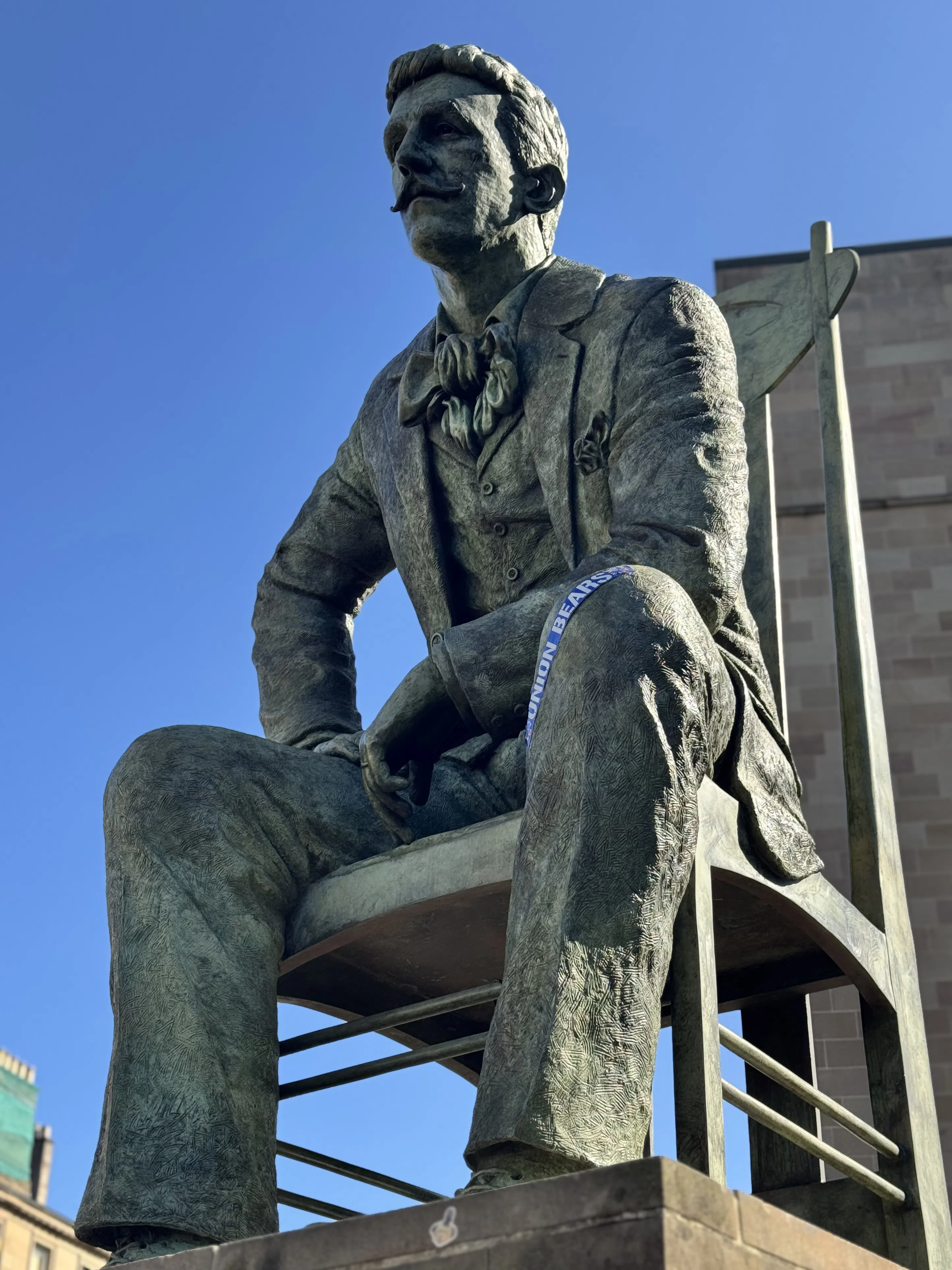 A seated bronze statue against a clear blue sky