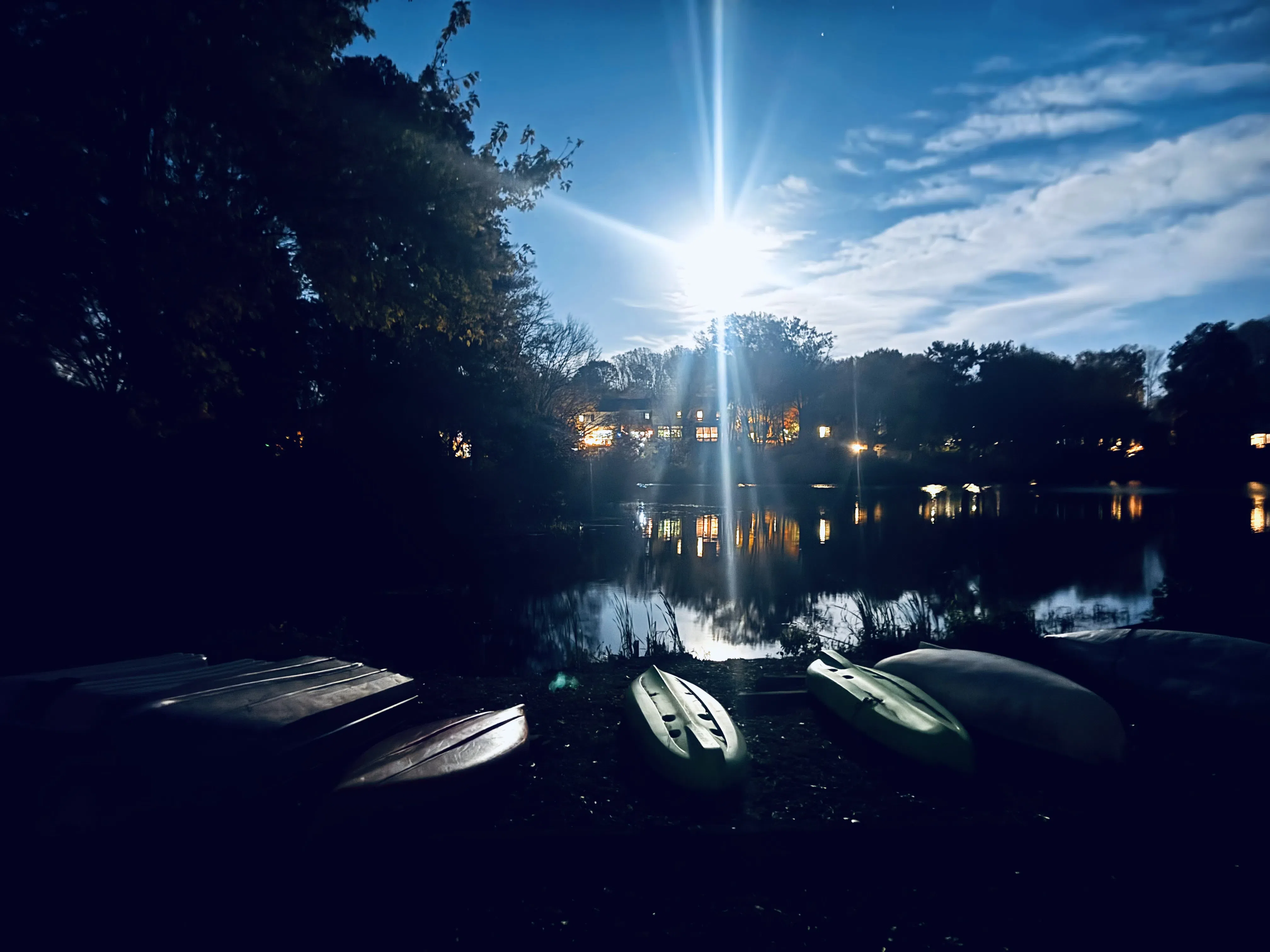 A dark lake scene with sunlight breaking above silhouetted trees