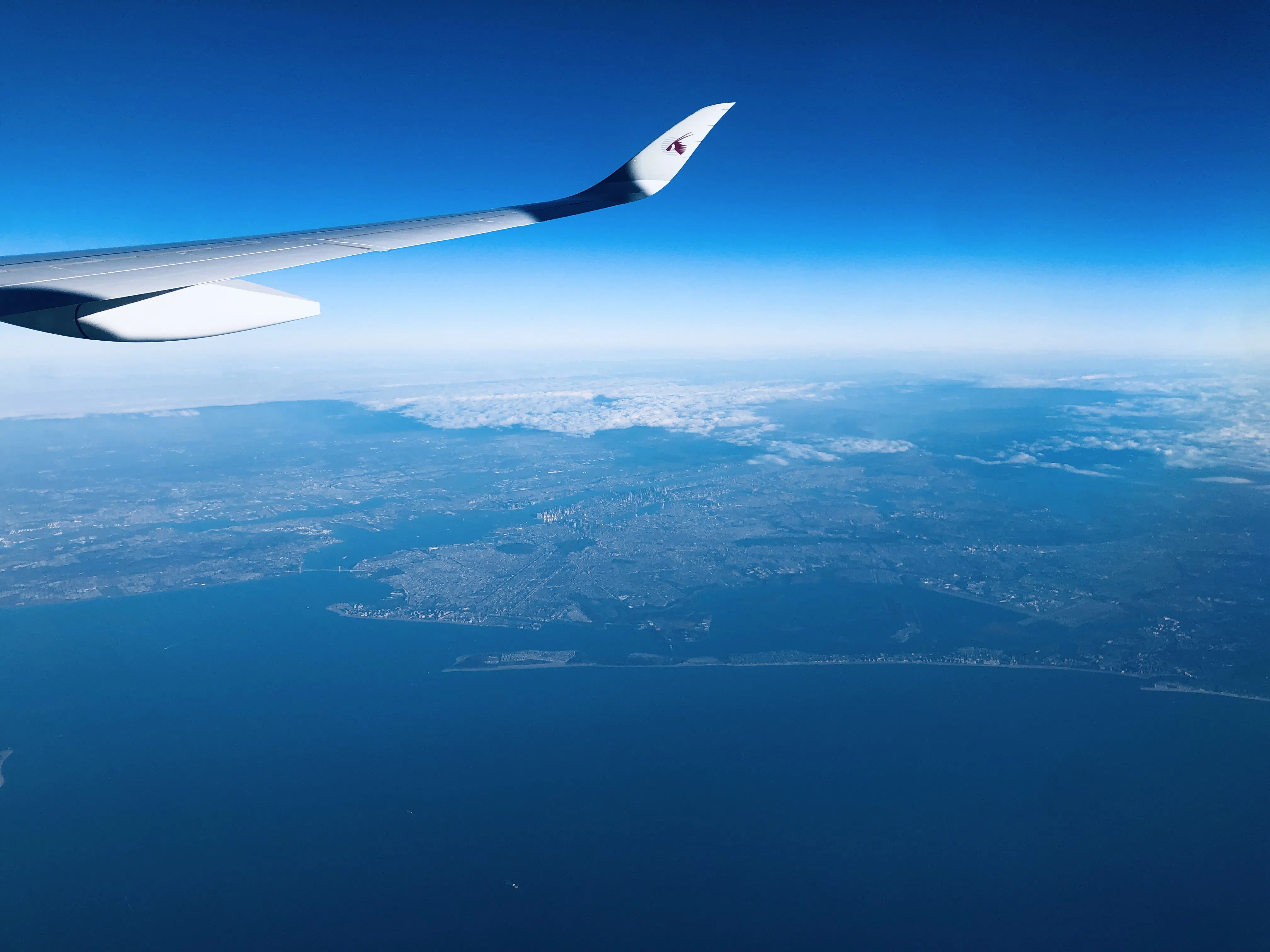 View from an airplane wing across coastline and mountains far below